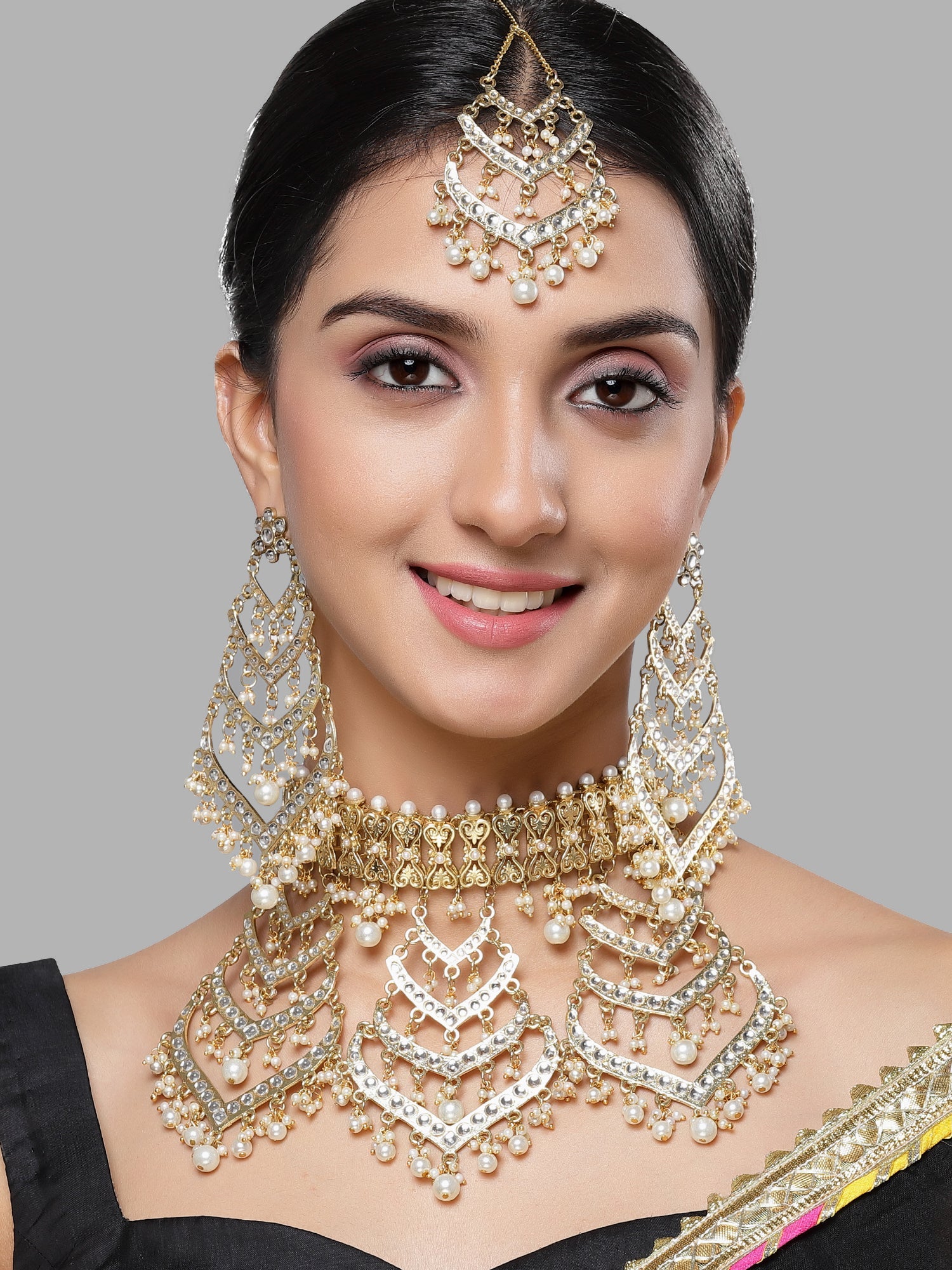 Woman wearing elaborate gold and pearl jewelry set against a gray background